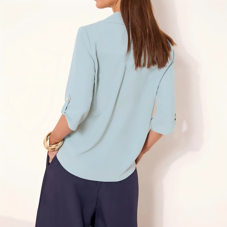 Light blue women’s collared V-neck blouse with three-quarter roll-tab sleeves and a curved back hem.